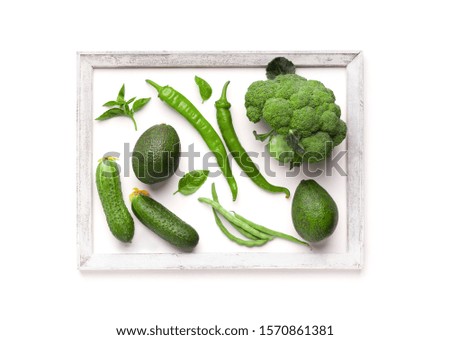 Creative picture of green vegetables inside wooden frame on white background, copy space