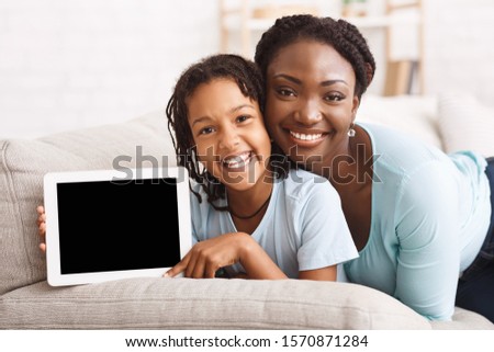 Best App. Black Mom And Daughter Smiling, Girl Holding Digital Tablet. Mockup, empty space