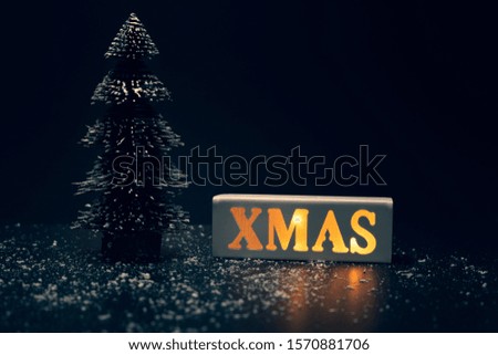 Merry christmas,xmas and celebration concepts with xmas lightbox text and pine tree on dark background.winter season and anniversary day