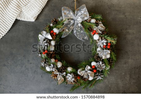 Christmas wreath of cones, fir branches and silver bows with red berries on a dark background, white plaid