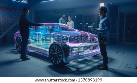 Group of Automobile Design Engineers Working on Augmented Reality 3D Model Prototype of Electric Car Chassis. Automotive Innovation Facility: 3D Concept Vehicle Frame Generated with 3D CAD Software. Royalty-Free Stock Photo #1570893199