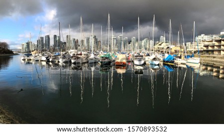 Colourful sail boats in marina with reflections in water under storm sky and Vancouver downtown buildings.  Heather Marina in False Creek. Vancouver. British Columbia. Canada.