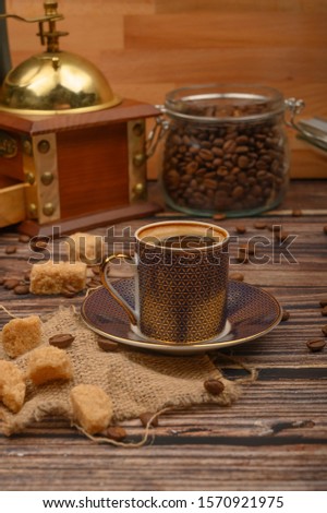 A Cup of coffee, coffee beans in a glass jar, brown sugar, coffee grinder on a wooden background.