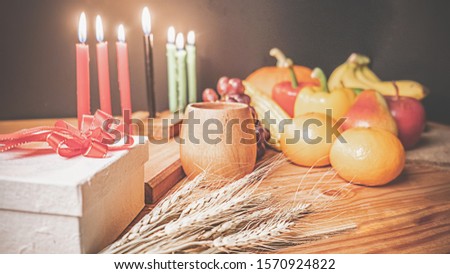 Kwanzaa holiday concept with decorate seven candles red, black and green, gift box, pumpkin,corn and fruit on wooden desk and background.