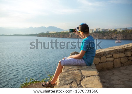 White young kid taking photos of great sunny beautiful landscapes using digital camera of mobile smartphone. Horizontal color photography.
