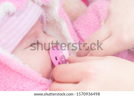Adorable infant girl wears a pink warm snowsuit and pacifier sleeps on a walk in a winter park. 