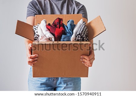 Unrecognizable woman holding box with clothes in it. close-up. Clothing donation. Royalty-Free Stock Photo #1570940911