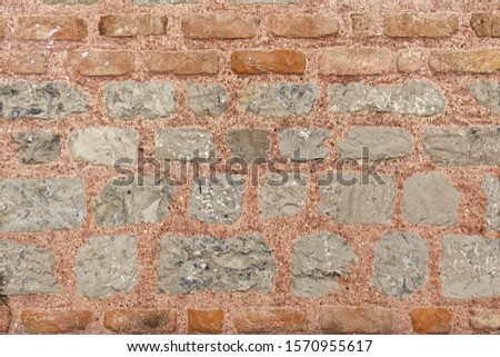 Gray stone wall texture with red fire bricks in the upper part. Pasted with red colored cement.