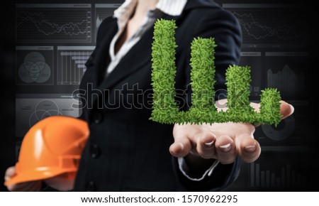 Businesswoman holds in palm green plant in shape of grow up chart. Woman engineer in business suit with orange safety helmet. Engineering and project management. Money saving and investing.