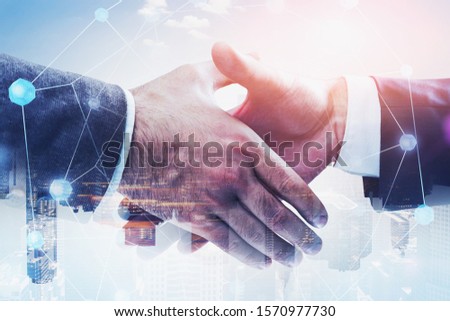 Two businessmen shaking hands in modern city with double exposure of network interface. Concept of partnership and hi tech startup. Toned image