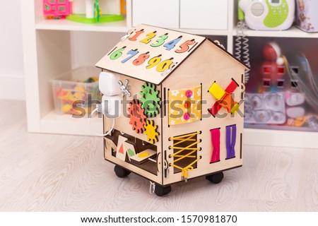 Wooden busy board house - educational toy for children, consisting of multi-colored wooden puzzle pieces, maze, gear, sorter,a lock with a key, roller, bell. Children's education.
