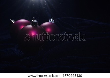 Three purple Christmas baubles on black velvet cloth in dark, light coming from above
