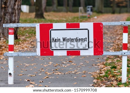 A red and white sign on a footpath at the entrance of a park in Nuremberg informs  Kein Winterdienst (in Englisch: no winter service ). Seen in Franconia / Bavaria in Germany in November.