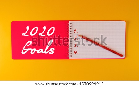 Open pink notebook on yellow background. 2020 goals list.