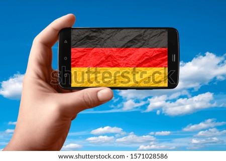 Germany flag on the phone screen. Smartphone in hand shows a flag on a background of the sky with clouds. Mobile photography.