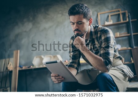 Photo of handsome serious guy holding e-reader website checking email online orders think how to improve service wooden business industry owner woodwork store indoors