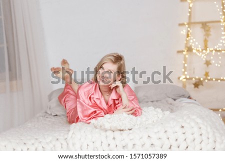 girl, blonde lies on the bed in pink pajamas, on the face of emotions, on the background of New Year's lights and garlands 