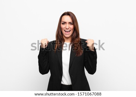 young pretty businesswoman feeling happy, surprised and proud, shouting and celebrating success with a big smile against white wall