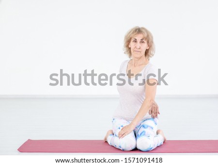 Portrait of a senior woman doing yoga at home, stretching exercises. Empty space for text