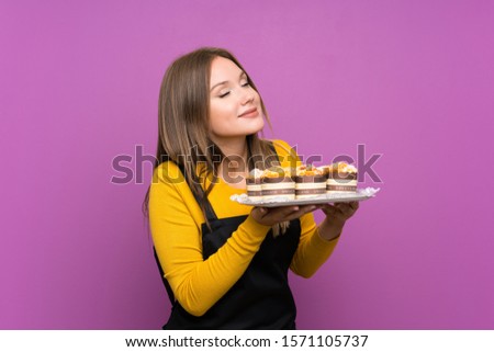 Teenager girl holding lots of different mini cakes over isolated purple background