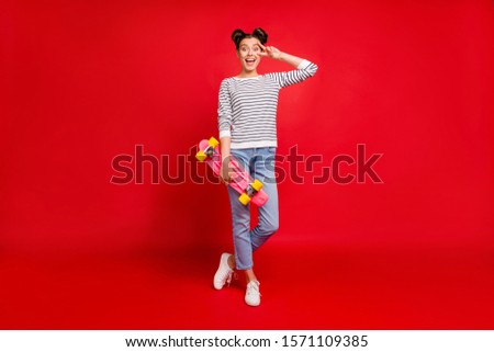 Full size photo of cute teen girl have sportive weekends hold pink skateboard make v-signs feel content expression wear white denim jeans outfit sneakers isolated red color background