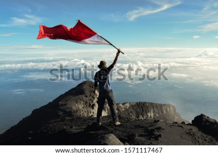 A man flying a red and white flag on the highest land of the island of Sumatra. Kerinci Mountain 3805 masl Royalty-Free Stock Photo #1571117467
