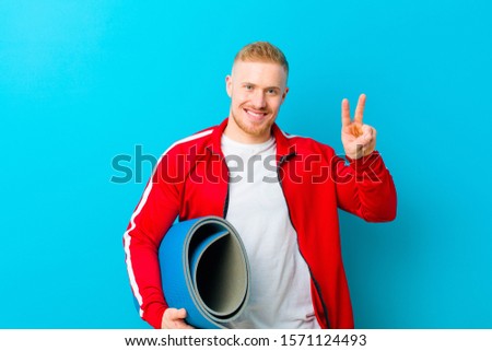 young blonde man wearing sports clothes  against blue background. fitness concept