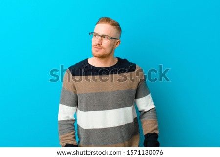 young blonde man looking puzzled and confused, wondering or trying to solve a problem or thinking against blue background