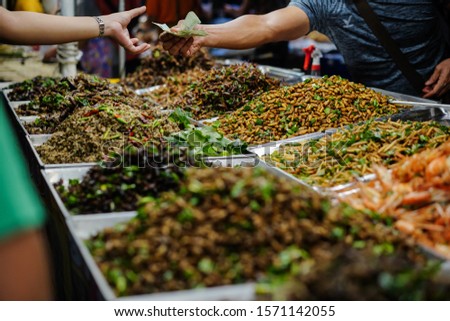 Focus on fried insect streetfood with unidentify hand buy and selling insect streetfood in Thailand market.