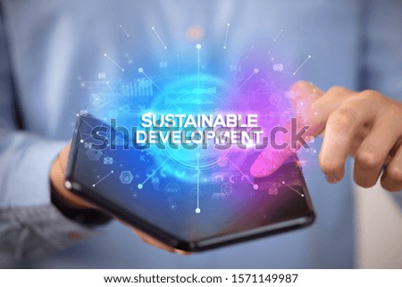 Businessman holding a foldable smartphone with SUSTAINABLE DEVELOPMENT inscription, new business concept