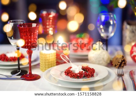 Beautiful table setting for Christmas party or New Year celebration at home. Cozy room with a fireplace and Christmas tree in a background. Xmas time with family and friends.