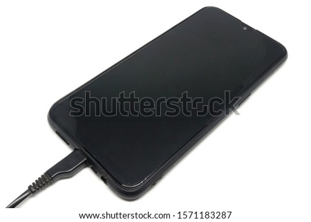 The black smartphone has a large screen made of glass. There is a black plastic usb cable plugged in. The bottom is placed on a white background.