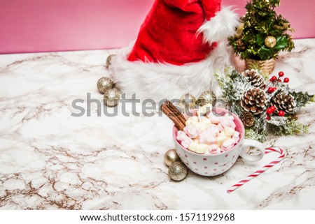 Pink white mug with marshmallows, Christmas tree, ornaments and Santa Claus hat on a marble and pink background
