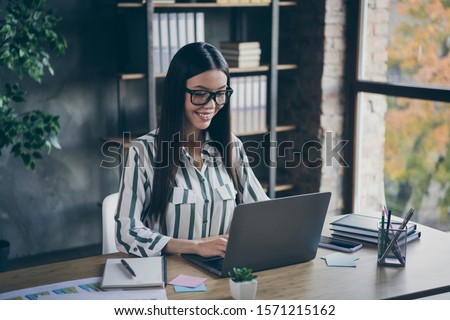 Photo of cheerful toothy beaming intelligent clever business girl looking into screen of notebook computer in spectacles concentrated on doing work qualitatively