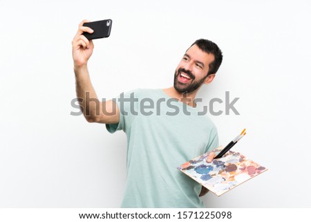 Young artist man holding a palette over isolated background making a selfie