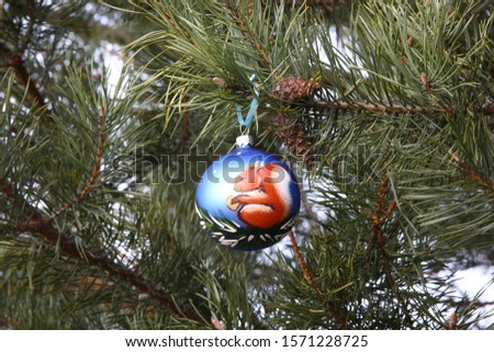 Close-up of a Christmas glass ball with hand-painted on a pine branch with cones.The picture shows a squirrel with a Golden nut sitting on a Christmas tree.The concept of a Christmas theme