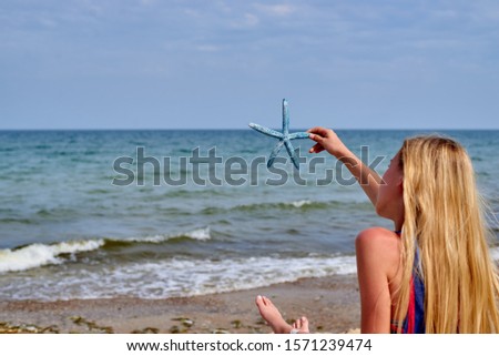 teenager girl with long blond hair on the beach holds a starfish