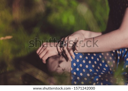 Women's hands. Polka dot dress. The girl is sitting in the grass. Summer.