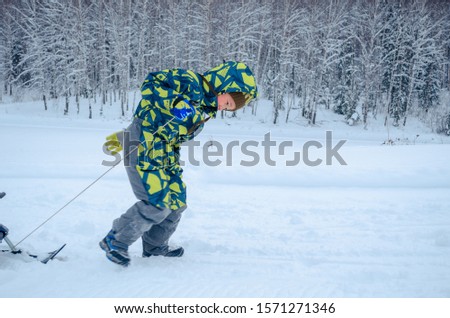Cute Asian child playing on white snow  in Siberia, riding a snow scooter. 
 With a smile of happiness.
