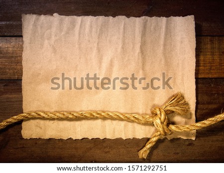 old sheet of parchment or paper lying on wooden boards and a coarse rope pulled into a nautical knot forming a frame