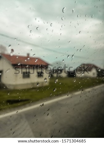 Cool raindrops on car's window while driving through village. Beautiful old houses in backgroung, grass, and sky.