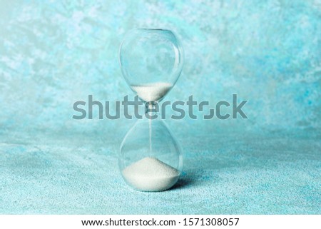 Time is running out concept. An hourglass with sand falling through, on a teal blue background with copy space