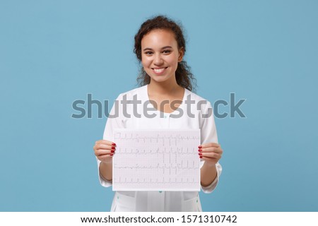 Smiling american doctor woman in medical gown hold electro cardiogram record, heart ekg chart of wave in paper isolated on blue background. Healthcare personnel medicine concept. Mock up copy space