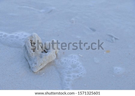 Heart-shape stone on the beach with wave bubbles.