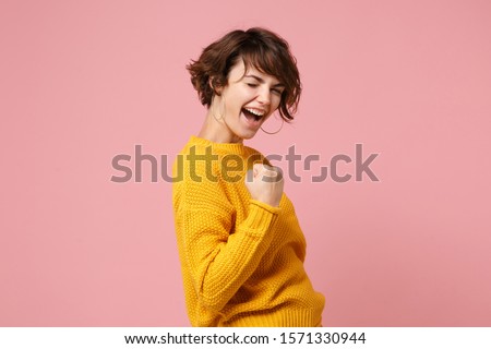 Side view of young brunette woman girl in yellow sweater posing isolated on pastel pink background studio portrait. People sincere emotions lifestyle concept. Mock up copy space. Doing winner gesture Royalty-Free Stock Photo #1571330944