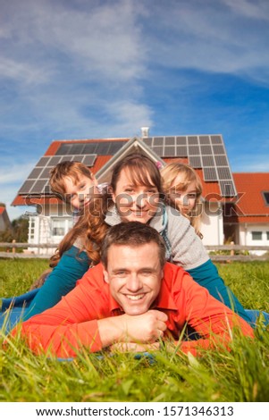 Happy family lying in grass in front of house with solar panels Royalty-Free Stock Photo #1571346313