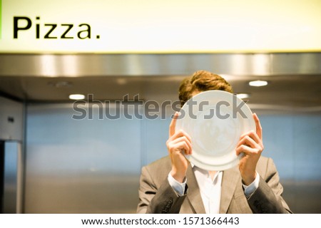 Businessman holding plate in front of his face in cafeteria