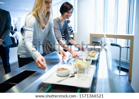 Businesswomen with lunch trays in work cafeteria Royalty-Free Stock Photo #1571366521