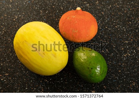 Colorful round vegetables and fruits on dark specle background. Pumpkin, melon and avocado still life. Colorful simple abstract composition. Food art concept, abstract arrangement.