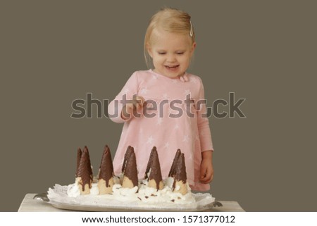 Studio shot of happy two years old girl standing behind a birthday cake